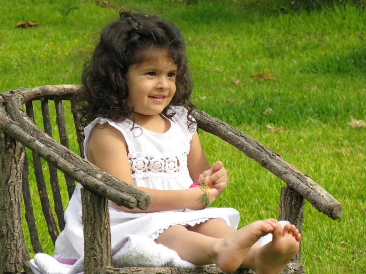 a small girl is sitting on the wooden bench