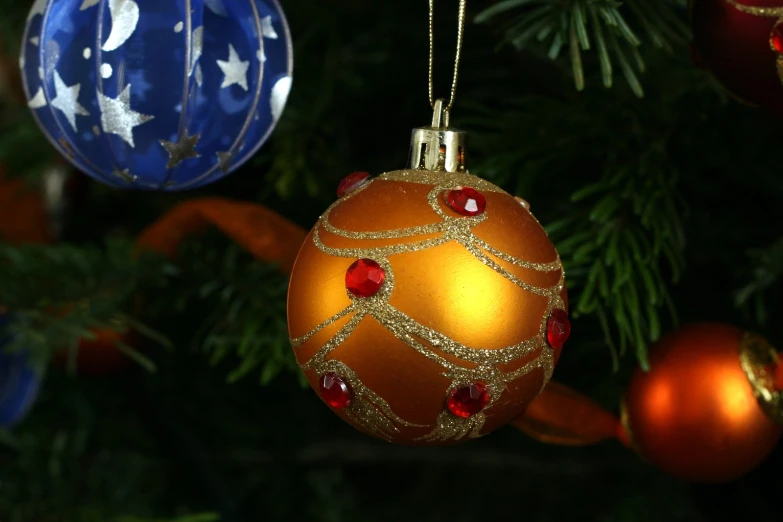 two blue and gold ornaments hang from christmas tree nches