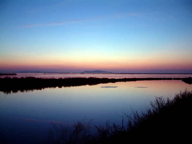 a sunset view of a lake and bridge in the distance