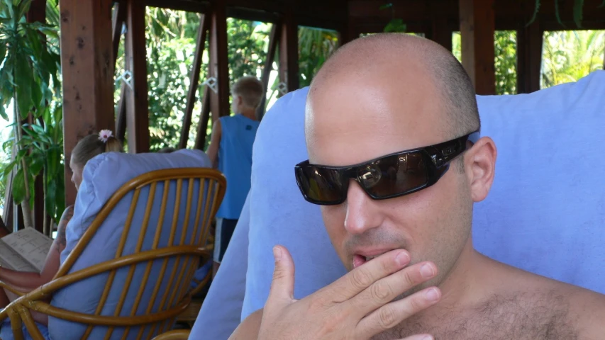 a man wearing sunglasses making a face while sitting on a beach chair