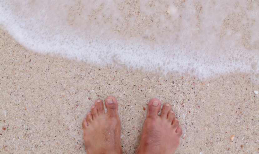 someone's feet on the sandy beach with white surf