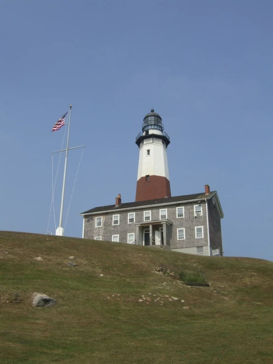 a lighthouse on a grassy hill, with an american flag flying above it