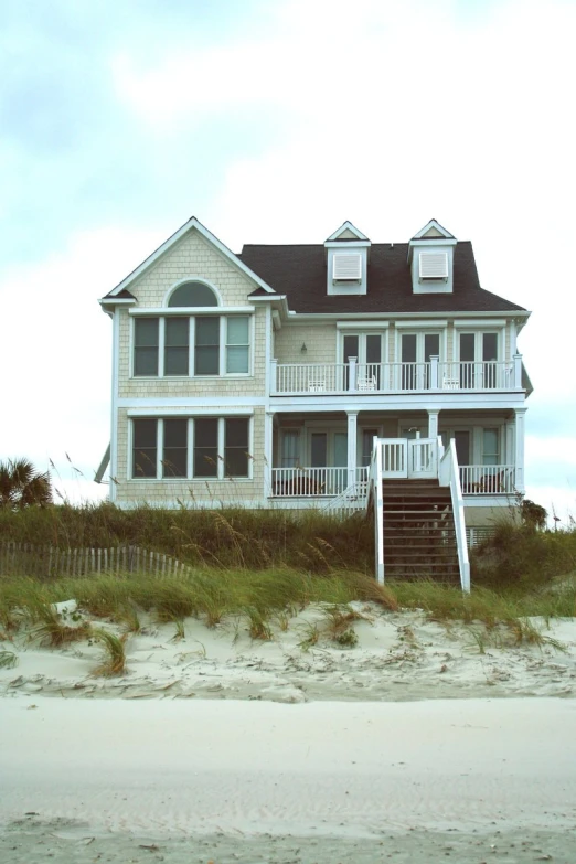 a large two story white house sitting on the side of a beach