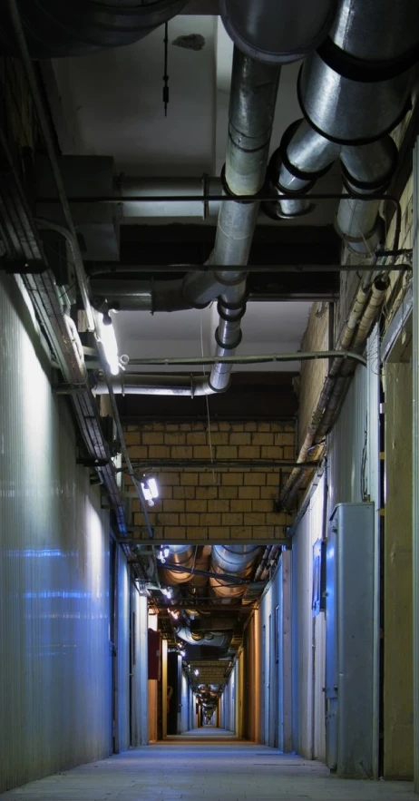 a hallway in the middle of a building filled with pipes and lights