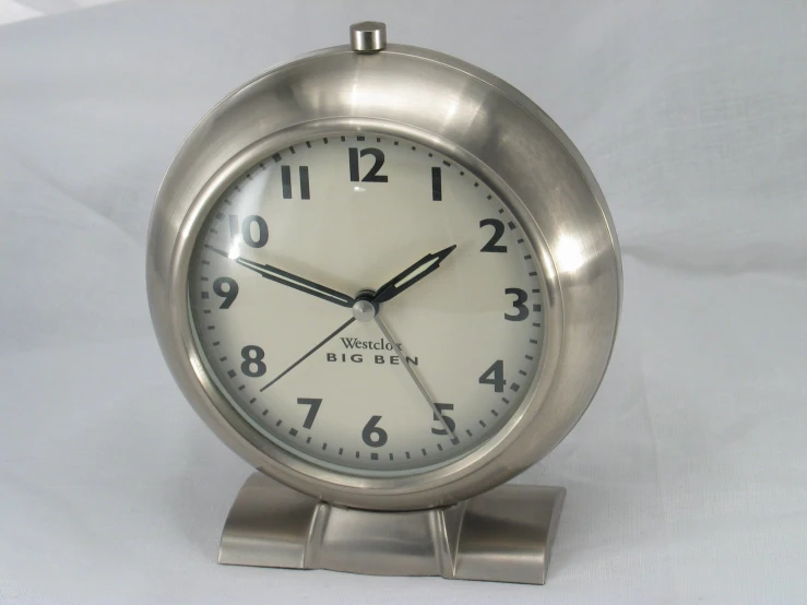 a small metal clock stands upright on a white background