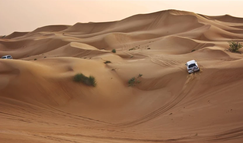 three trucks are driving in the middle of a huge sand dune