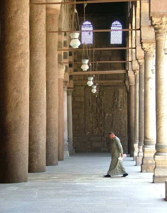 a man walking down a long building with columns