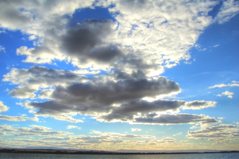 a lake with large clouds covering it with blue sky above