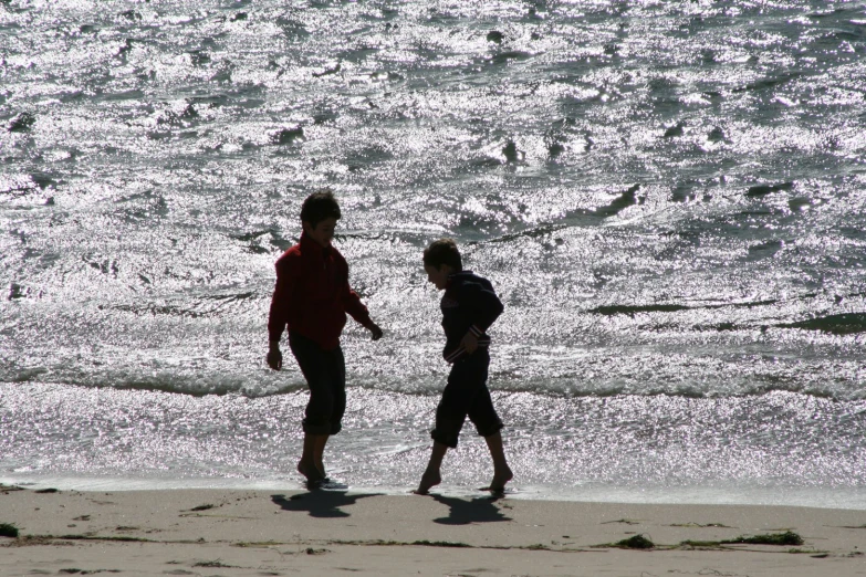 two people walking on a beach next to the water