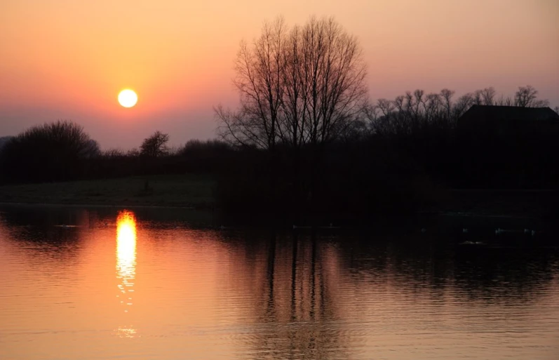 a sunrise on top of the water over a grassy field