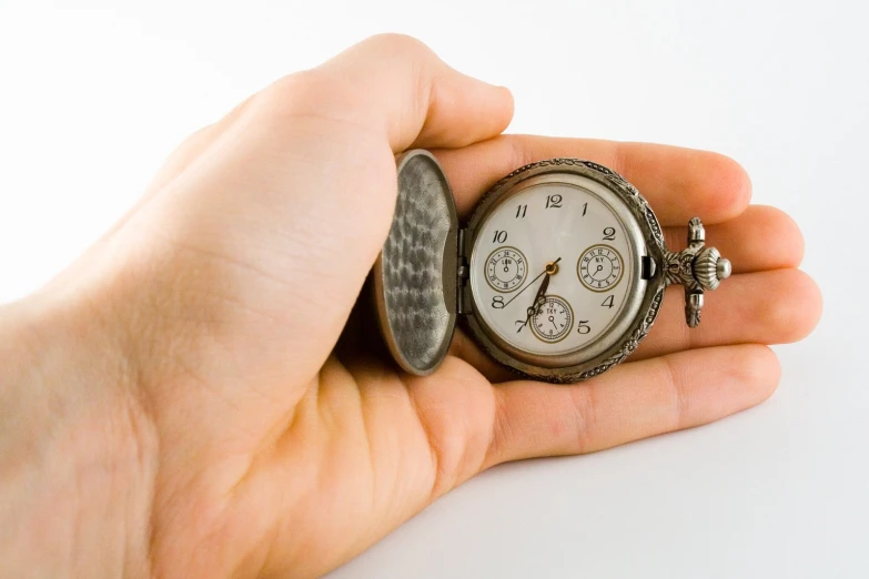 a person holds a small pocket watch in their hand