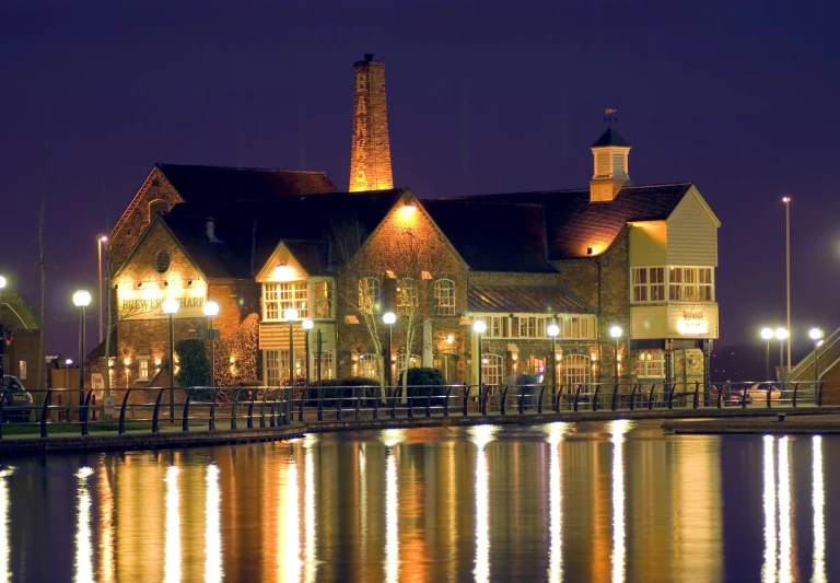 an old fashioned lit up building with a lake in front of it