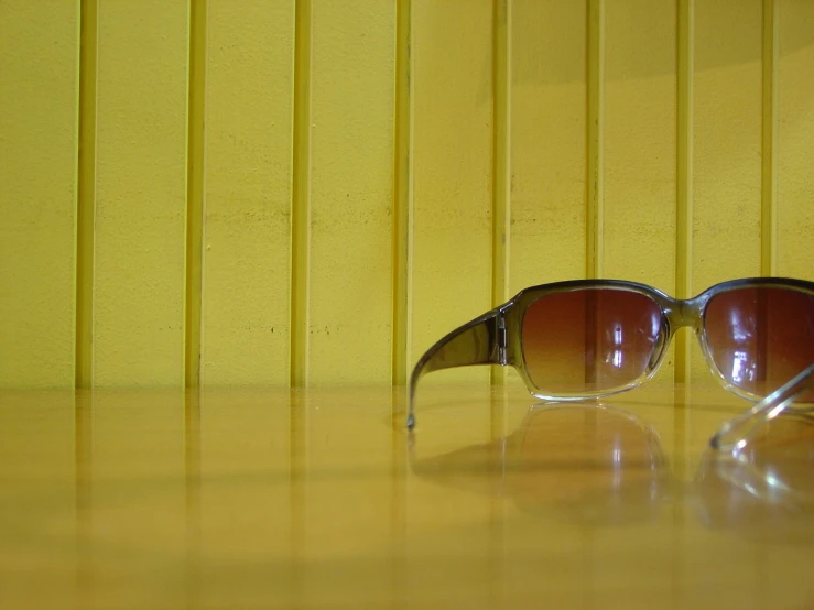 the sunglasses are on the wooden table in front of yellow background