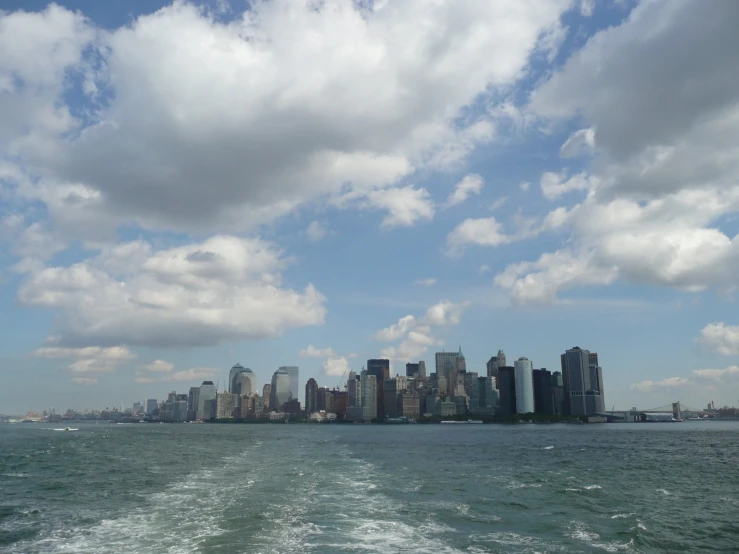 the cityscape on the water has white clouds above it