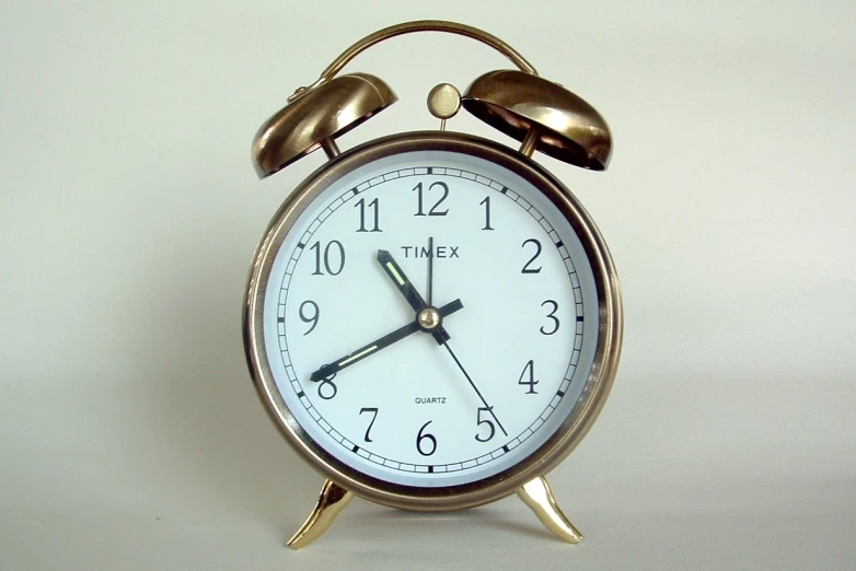 a gold alarm clock with a white face on a white background