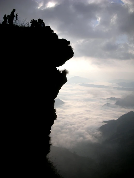 the silhouette of two people standing on a cliff overlooking a cloudy valley