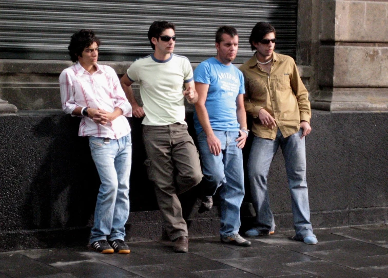 four males in casual clothing standing against a wall