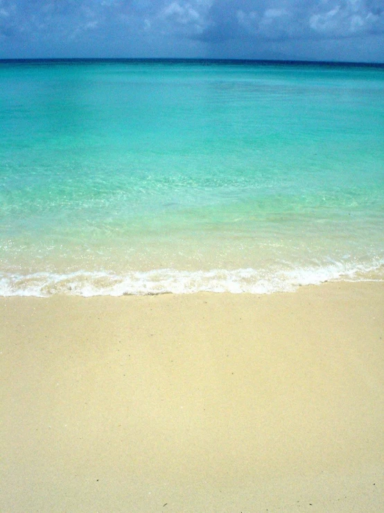 a sandy beach with some blue water and clouds in the background