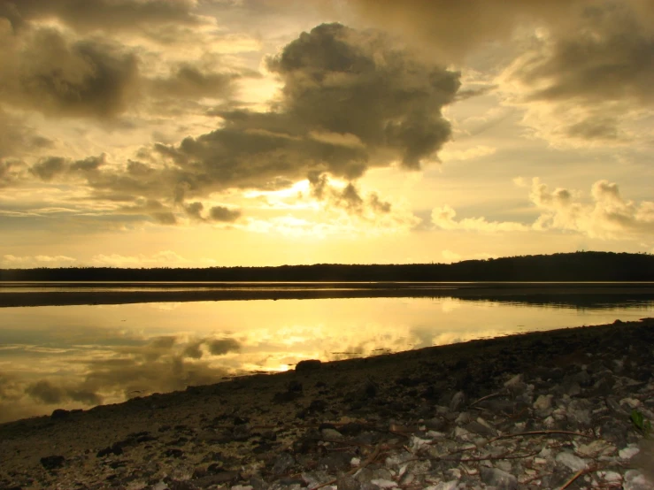 the sun setting over a body of water and a small hill with trees in it