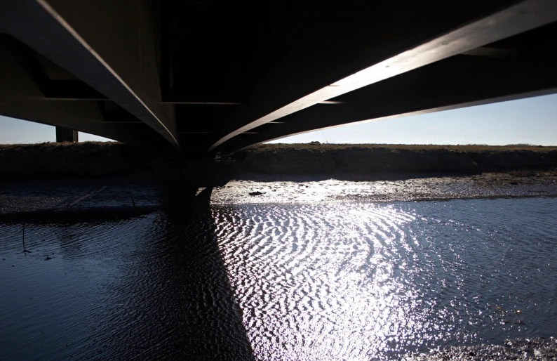 the sun reflects on the water and under a bridge