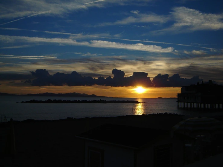 the sun is setting over the water with clouds