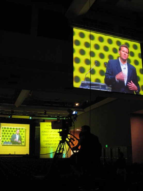 a po of the back of a television showing a man speaking on an indoor event