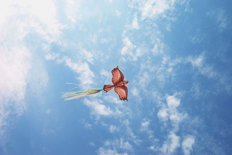 a red erfly flies through the blue cloudy sky