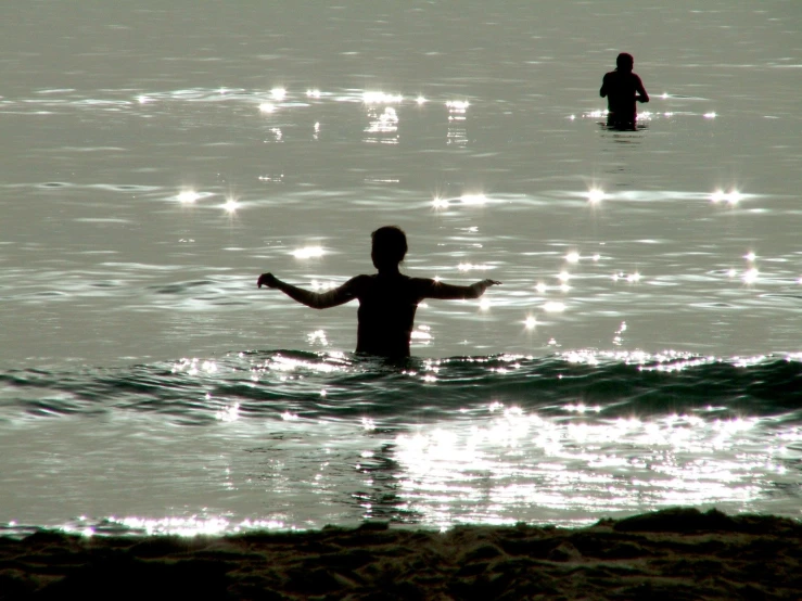 the silhouette of two people in the water near one another