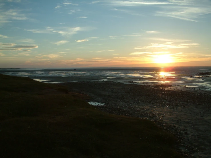 the sun rises over a beach and grassy area