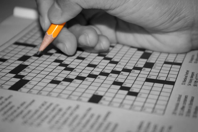 someone putting a pencil on the top of a crossword