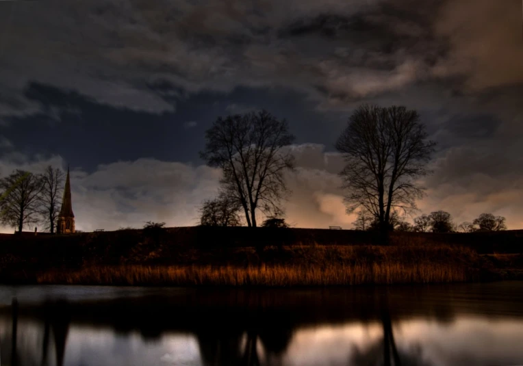 a lake with a dark sky at night, with a few clouds, trees and water