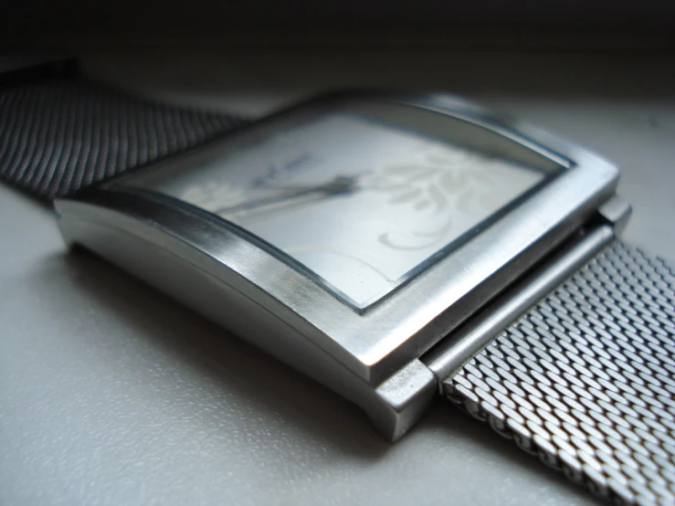 an elegant, silver square watch sitting on a tie