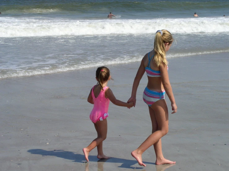 two little girls are walking together holding hands on the beach