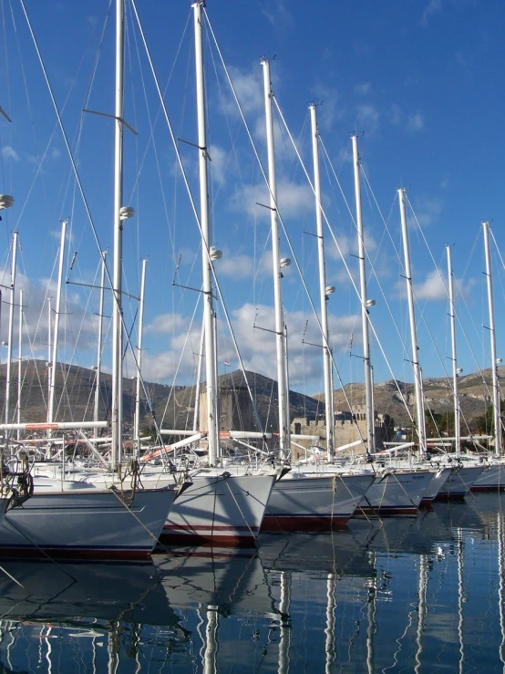 a line of sail boats in a harbor with mountains in the background