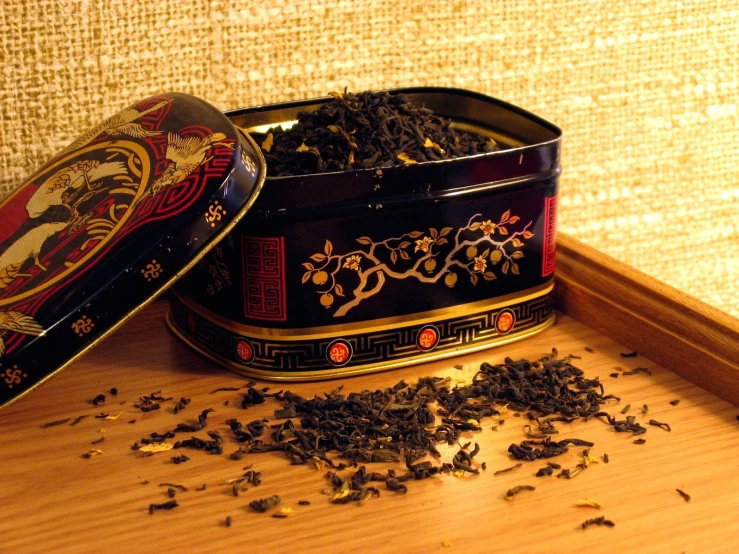 a wooden shelf with an open metal container and a black tea tin filled with dry cut leaves