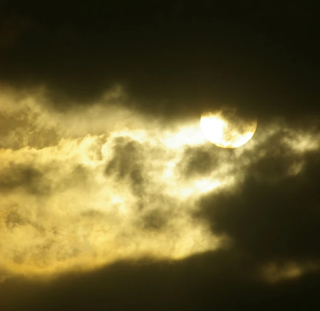 the sun shines behind dark clouds over water