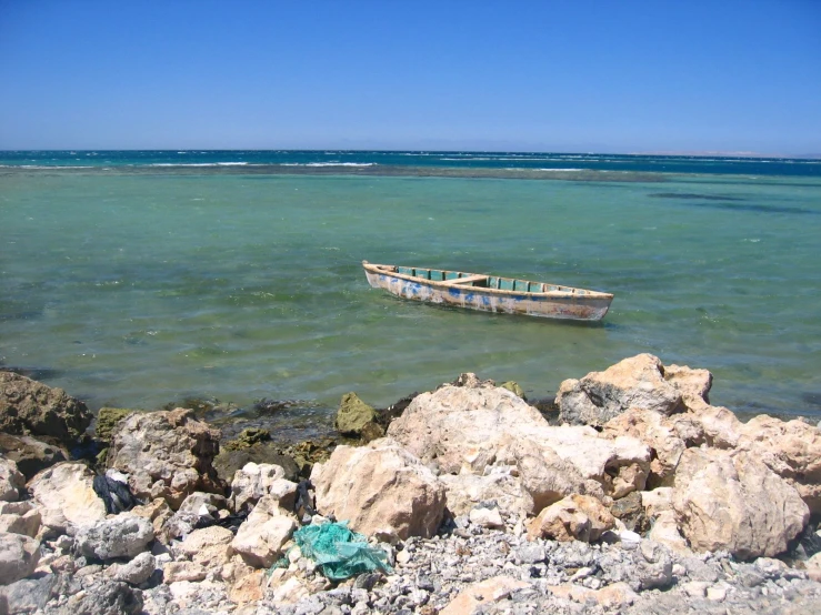 a boat sitting on the side of a beach near a rocky shore