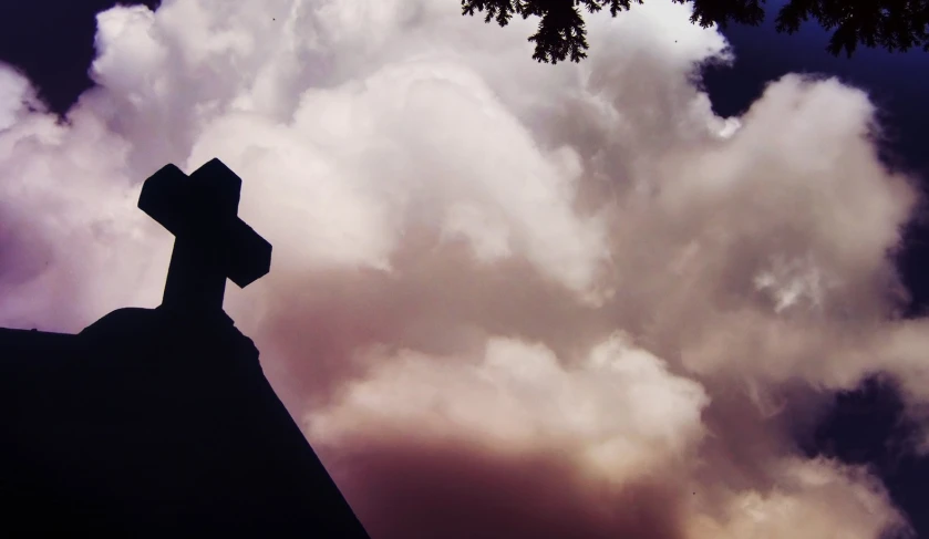 silhouetted cross on top of building and sky in background