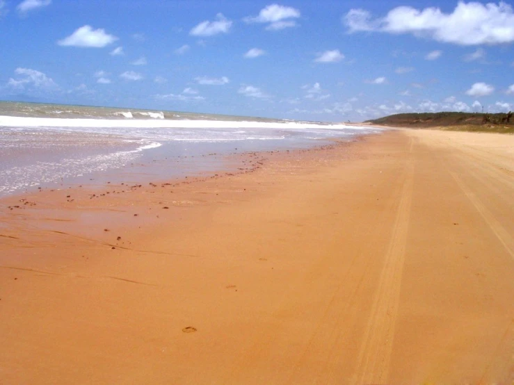 a beach area has water on the far side and a blue sky above