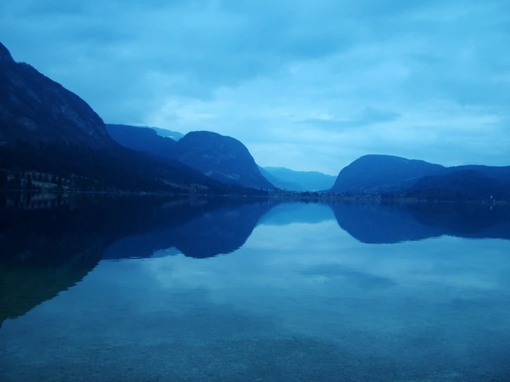 an empty lake near mountains under a cloudy blue sky