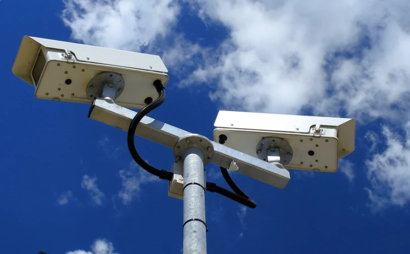 two security cameras are hanging from a pole