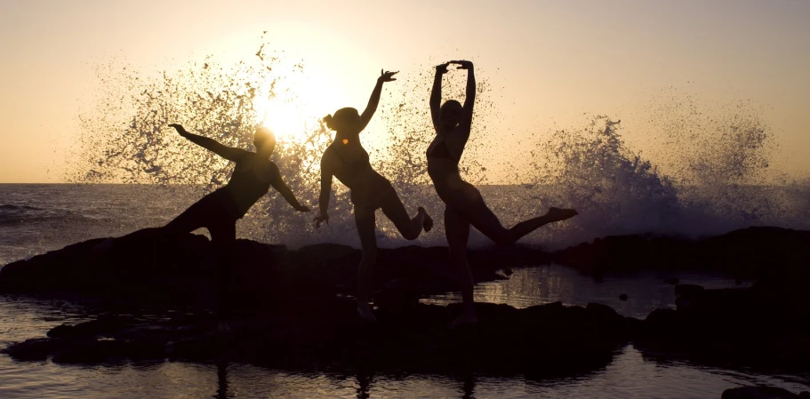 three people that are dancing on some rocks in the water