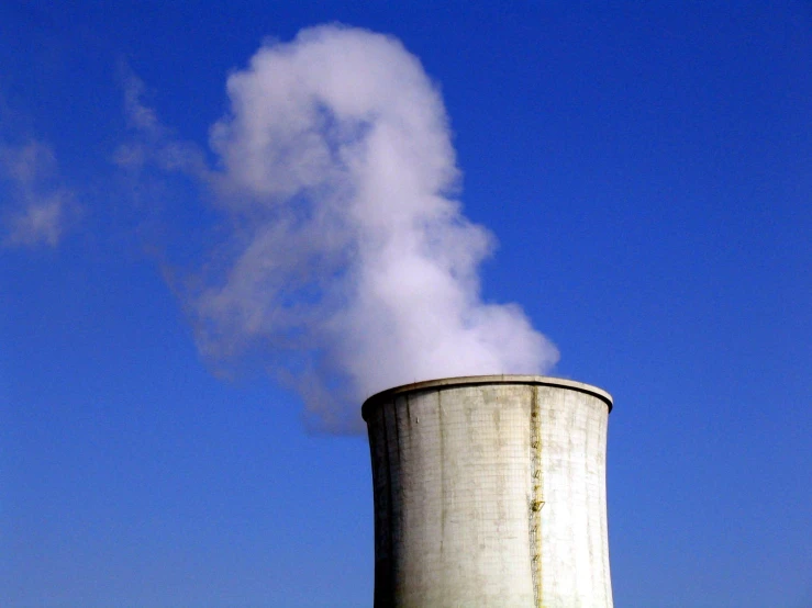 a large white smoke stack near trees and blue sky