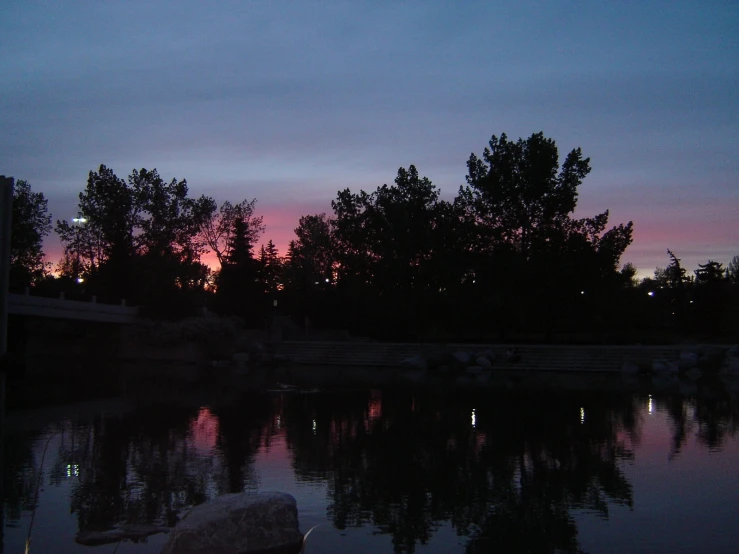 a dark sunset is reflected in a calm pond