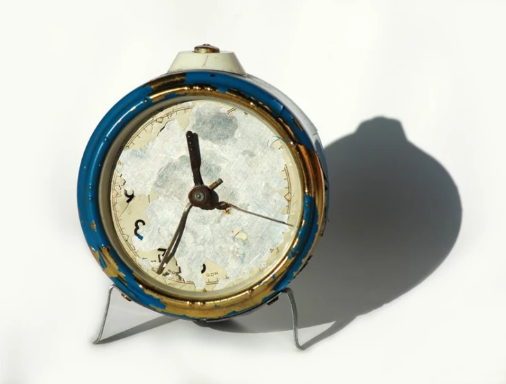 a very small and old style clock, set on a white surface