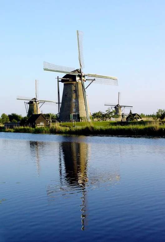 a windmill on the edge of a lake with a small herd of sheep nearby