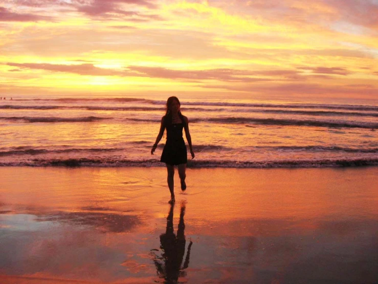 a woman walking on the beach at sunset