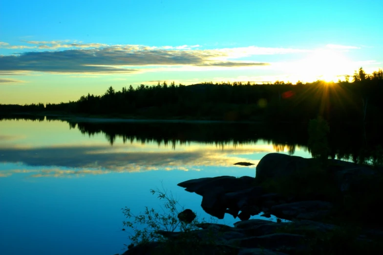 the sun setting over water with trees in the background