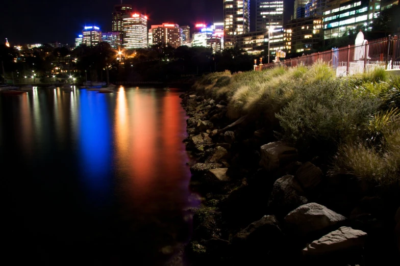 a city at night with illuminated buildings next to a lake