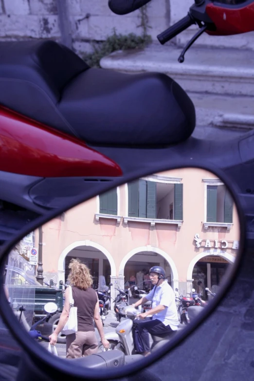 the side mirror of a motorbike and a couple of people riding